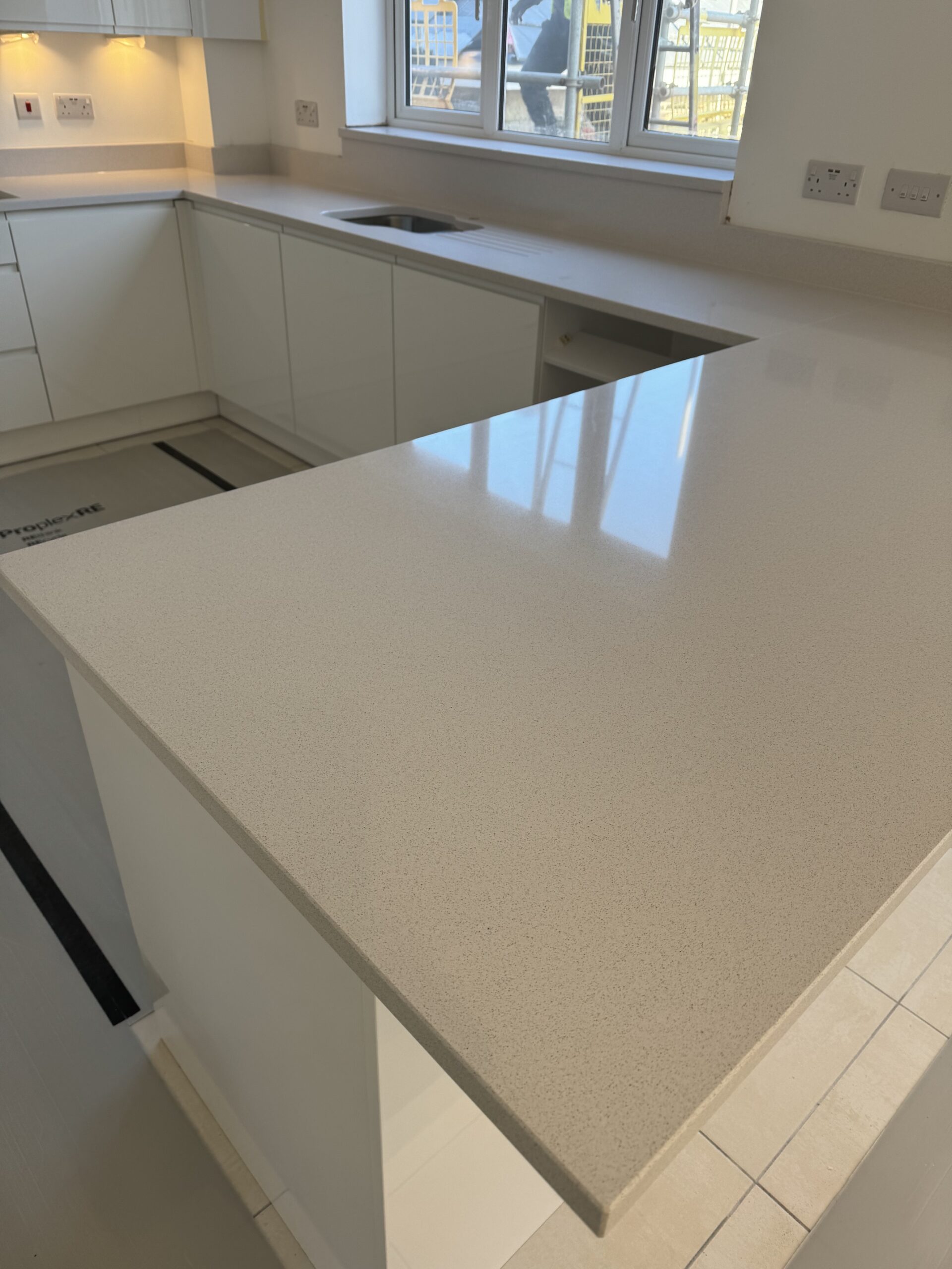 Beige flecked quartz breakfast bar with a 300 mm seating overhang and matching sink-area cladding in Leeds.