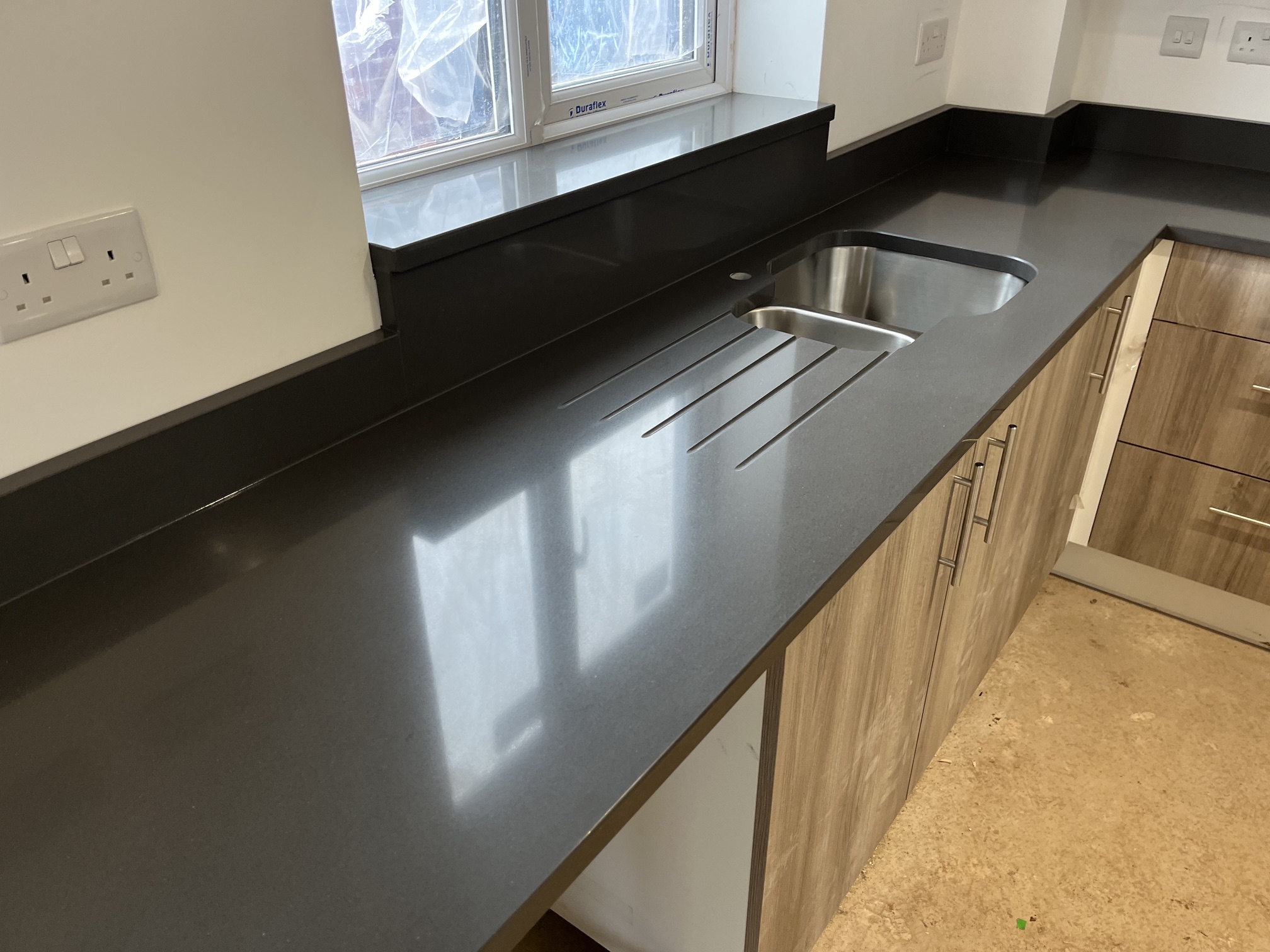 Brown quartz worktop with draining grooves, stainless steel undermounted sink and matching shelf and downstand in Derbyshire.