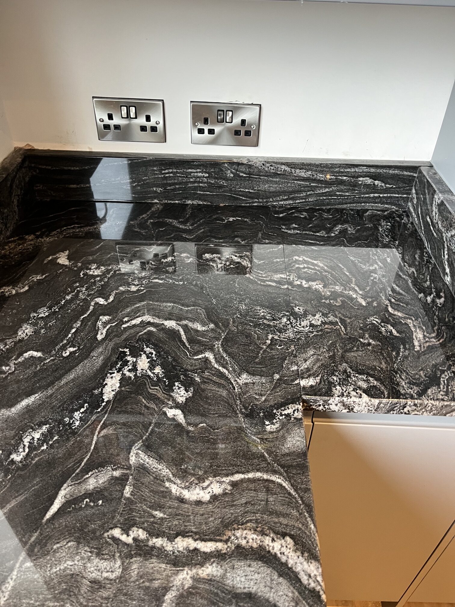 High-gloss black-and-white granite worktop with veining matched across an L-shaped joint and matching upstands in Chesterfield.