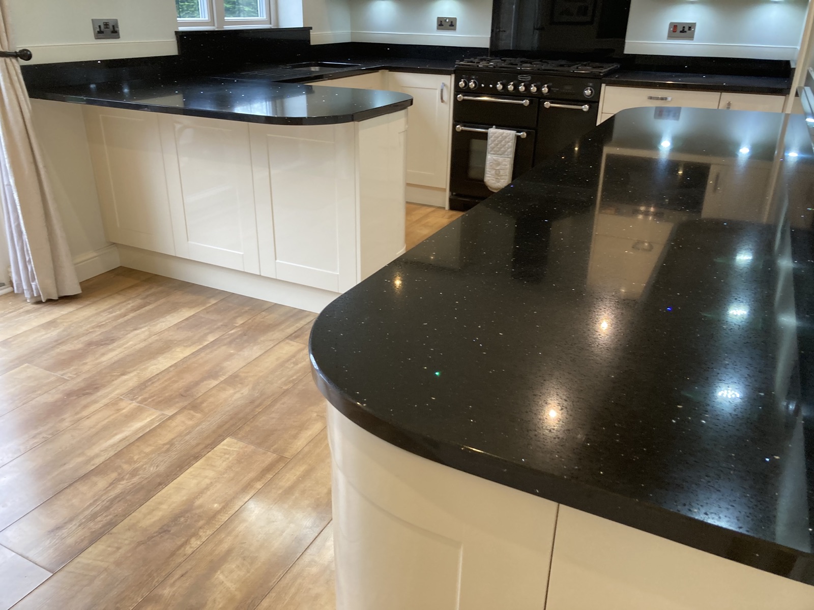 Stellar Black quartz worktops with mirror flecks and a curved breakfast bar, paired with high-gloss cream kitchen units in Oldham.