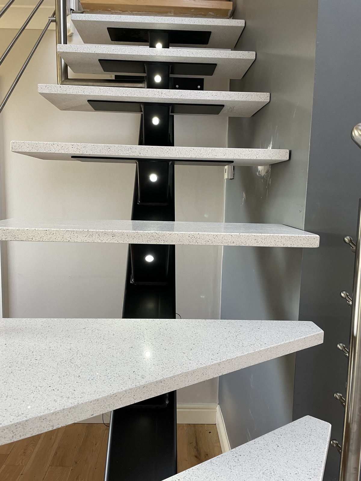 View up a Stellar White quartz staircase showing shaped treads and an illuminated steel central support.